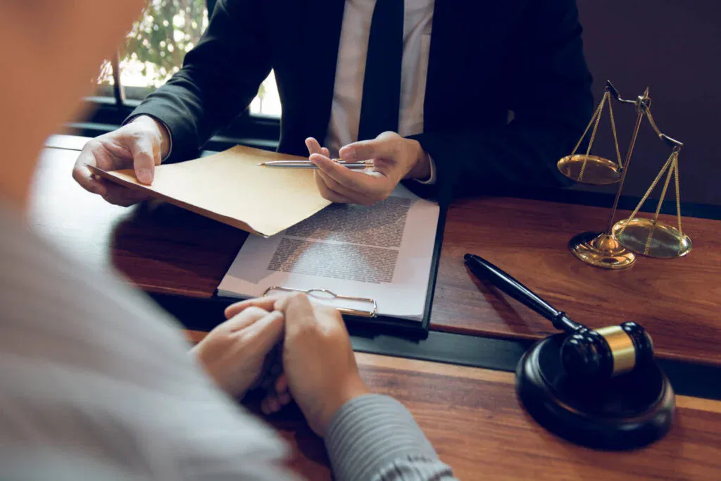 Steuerstrafrecht Anwalt berät Mandanten am Schreibtisch, mit Aktenmappe, Dokumenten, Waage und Richterhammer im Büro